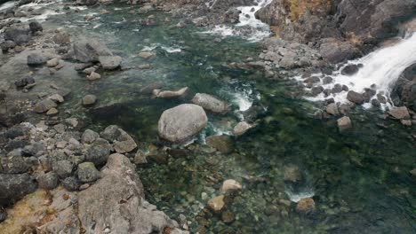 A-waterfall-joining-with-a-shallow-mountain-river-in-theBrattlandsdalen-valley,-Norway