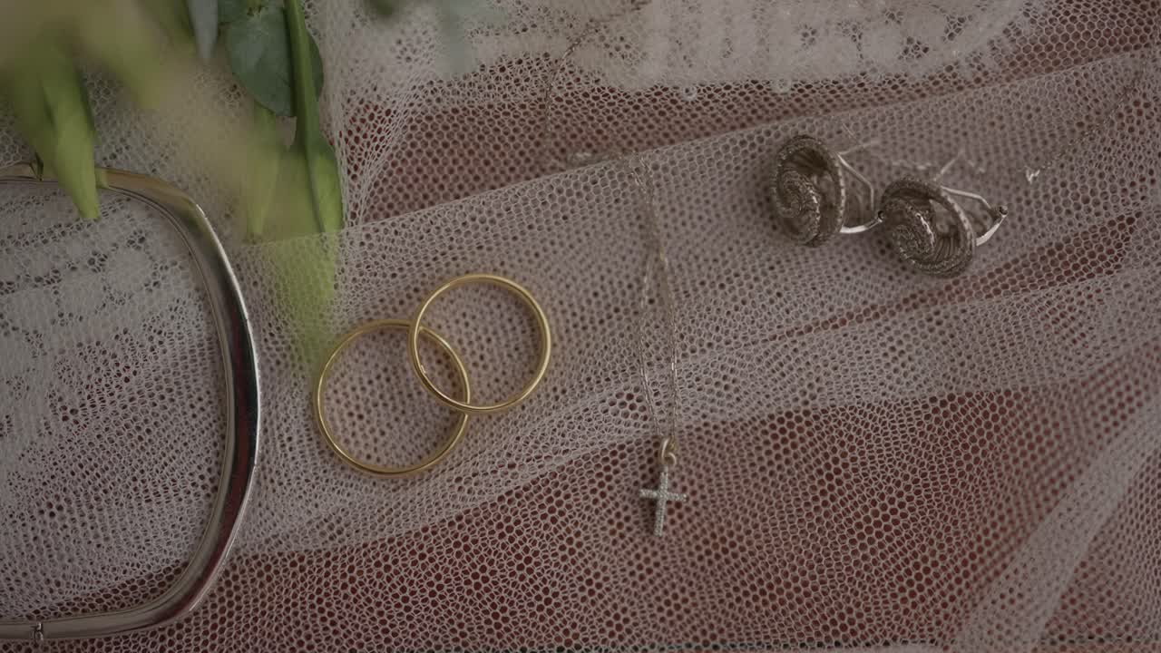 two golden wedding rings beside a silver cross necklace placed on soft lace fabric