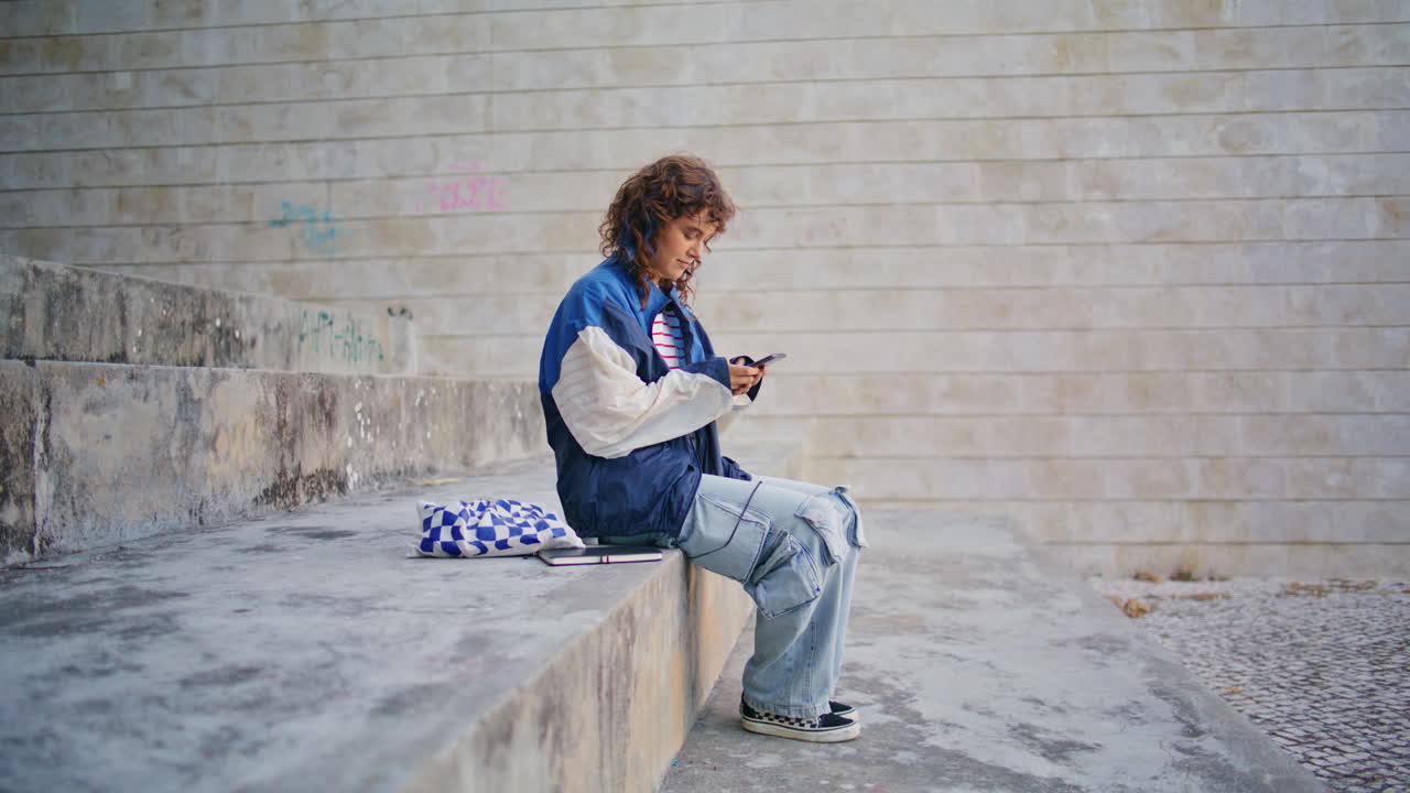 chica rizada leyendo un mensaje de teléfono móvil en la calle. adolescente navegando por el teléfono inteligente