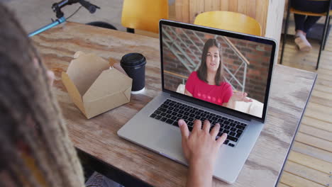 mujer tomando un bocadillo mientras hace una videollamada en una computadora portátil en una cafetería