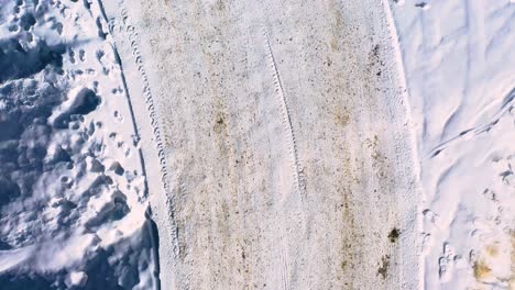 snow-covered winding road neighborhood or long driveway with tire tracks and mud streaks packed in with footprints