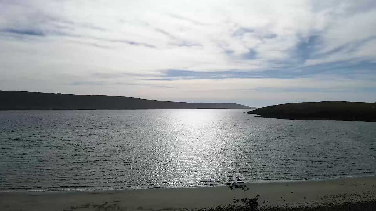 Eine ruhige Küstenlandschaft einfangen, mit wunderschön reflektierendem Sonnenlicht auf dem ruhigen Meer, unter einem teilweise bewölkten Himmel