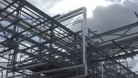 low angle shot looking up at a dense and complex network of industrial pipes and steel support structures against a cloudy sky, castets, france