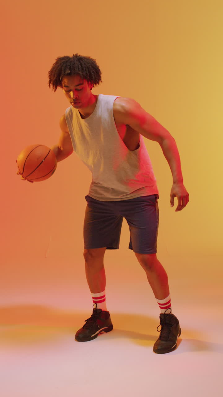 video vertical de un jugador de baloncesto masculino biracial con una pelota en un fondo naranja