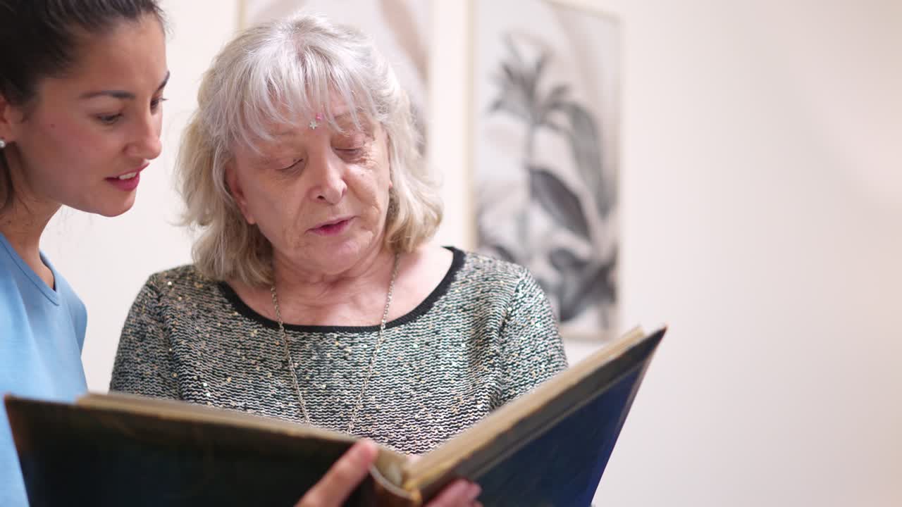 Elderly Woman and Caregiver Share Memories While Looking at a Book