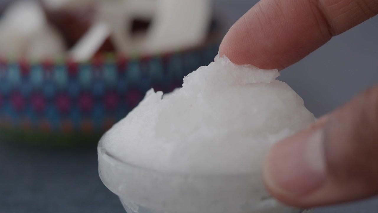 ガラスのボウルに入ったココナッツオイルに触れる指