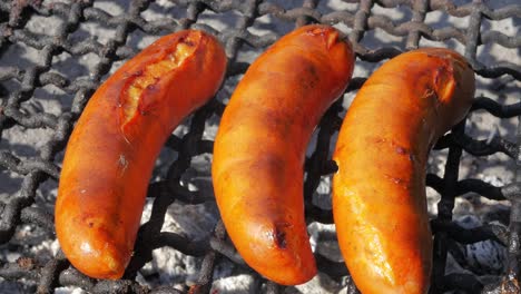 Three-sausages-being-cooked,-on-a-simple-concrete-outdoor-grill
