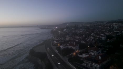 Vista-Aérea-De-La-Ciudad-De-Cascais-En-Portugal,-Drones-Vuelan-Sobre-La-Costa-Con-Algunos-Autos-Conduciendo-Y-Pequeñas-Olas-Rompiendo-En-La-Costa