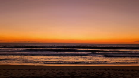 Slow-motion-shot-of-colorful-sky-above,-with-ocean-waves-crashing-along-the-tropical-beach-during-evening-time