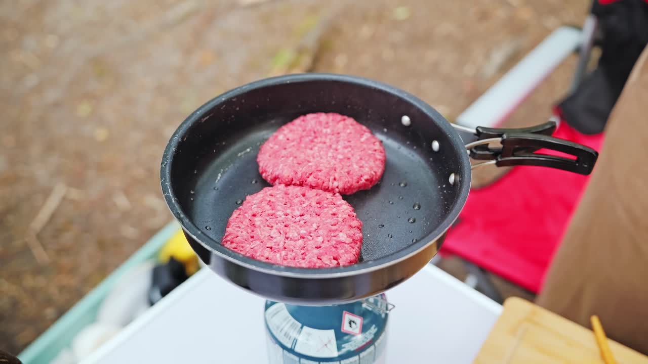 Open flame heats burger patties on portable stove in remote outdoor site