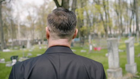 back view of a man in black suit walking in a graveyard