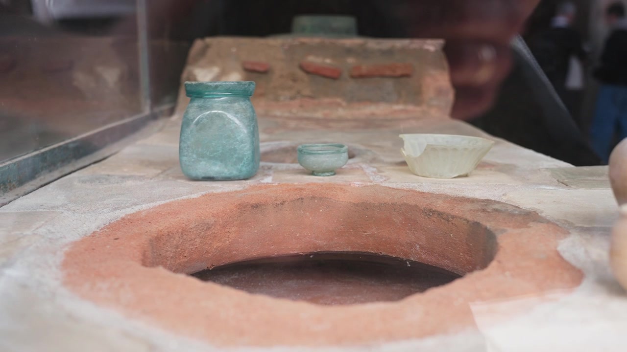Antica ceramica romana esposta all'interno di un termopolio di Pompei, con brocche di ceramica, piccola tazza, apertura di dolia e una luce interna soffusa in stile museale