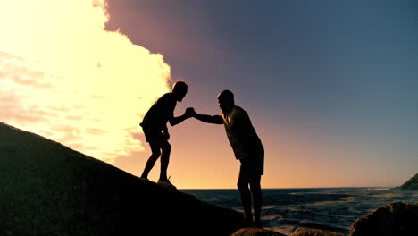 silhouette of people helping each other climb on the beach at sunset