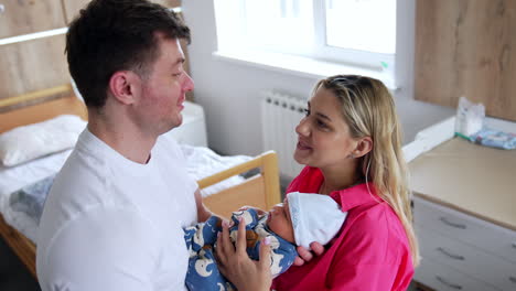 caucasian parents stand in the hospital ward holding their baby. happy couple talk smiling. high angle view.