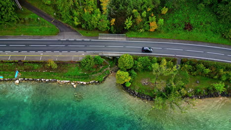 Aerial-view-of-a-black-car-traveling-through-the-scenic-road-close-to-the-shore-of-Attersee-Lake,-Salzkammergut,-Austria