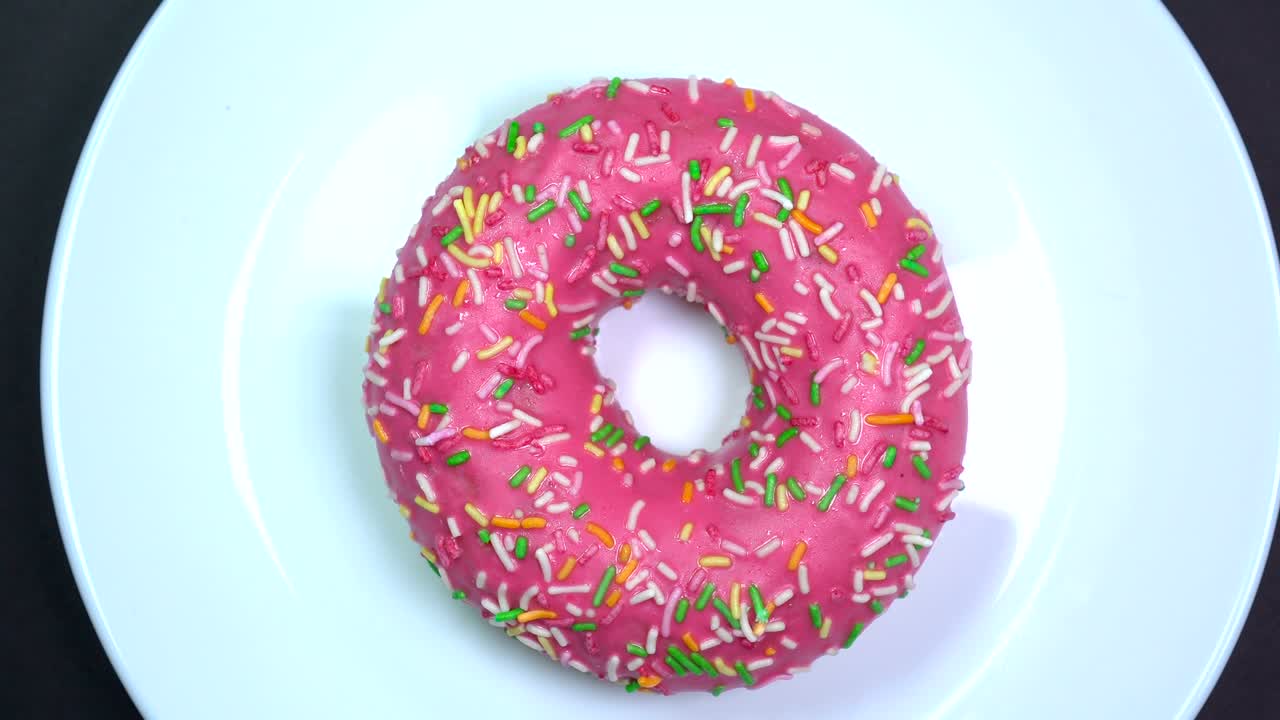 brillantes y coloridas salpicaduras de rosquilla, tiro macro, girando lentamente en un plato sobre un fondo oscuro.