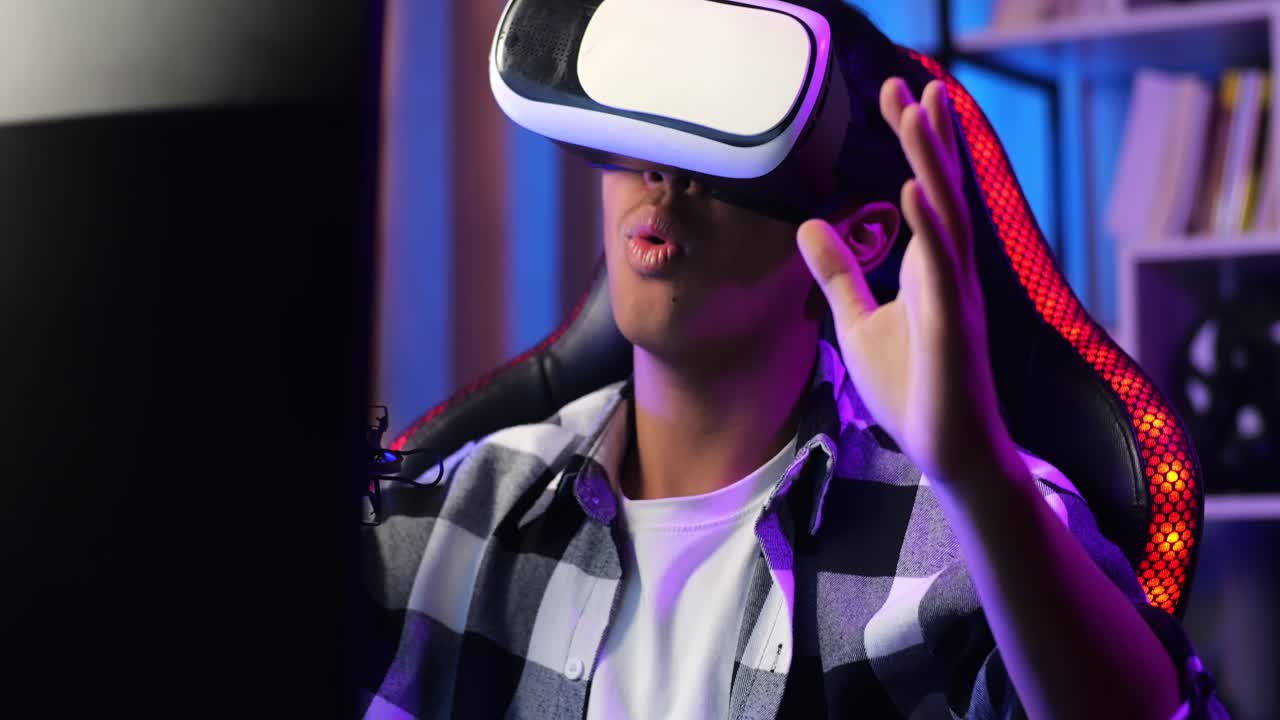 Close Up Of Asian Boy Streamer Playing Game, Double Touching, And Swiping Experience Virtual Reality In Futuristic Goggles. Player Touching Air Panel. Personal Computer On Desk Illuminated By Rgb Led Strip Light