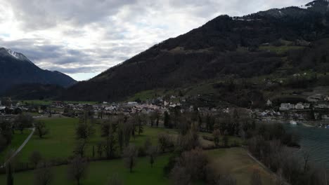 Aerial-pan-above-peaceful-village-at-base-of-mountains-overlook-lake