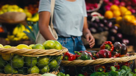 cliente femenina en el puesto del mercado eligiendo pimientos y limones