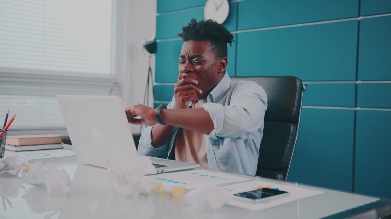 Young african american man typing on laptop and falls asleep sits in office