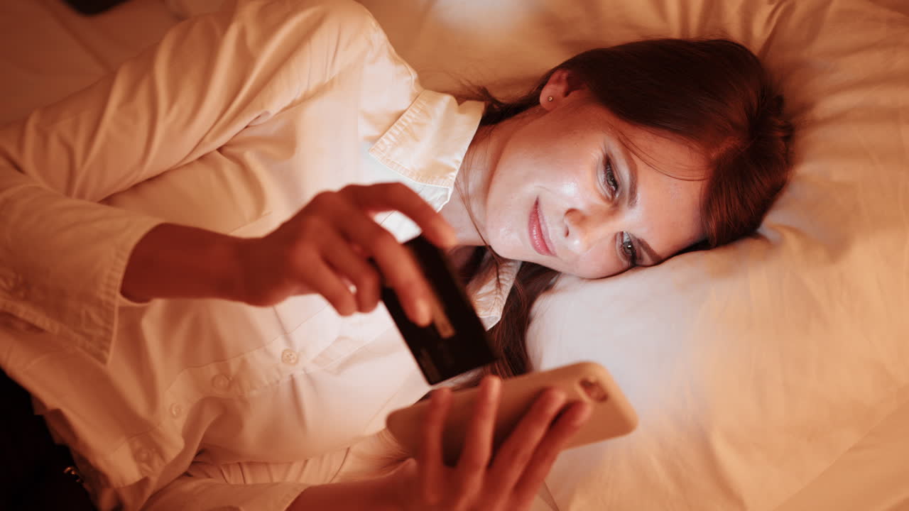 밤에 침대에서 스마트폰과 신용카드를 사용하는 여성