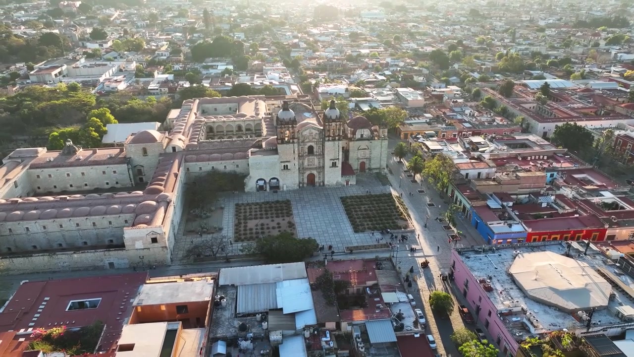 Una mozzafiato vista aerea cinematografica con drone che cattura lo storico Templo de Santo Domingo de Guzmán e il suo ex monastero adiacente, circondato dalla colorata griglia stradale coloniale di Oaxaca City.