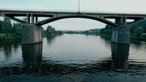 smooth drone footage - flying low above water under an arc bridge over rippled vltava river with reflection