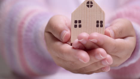 detail of female hand holding small wooden block residence in hands - real estate acquisition concept