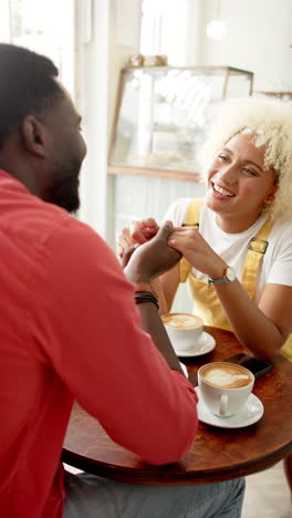 vertical video: african american couple holding hands, enjoying coffee and smiling at cafe