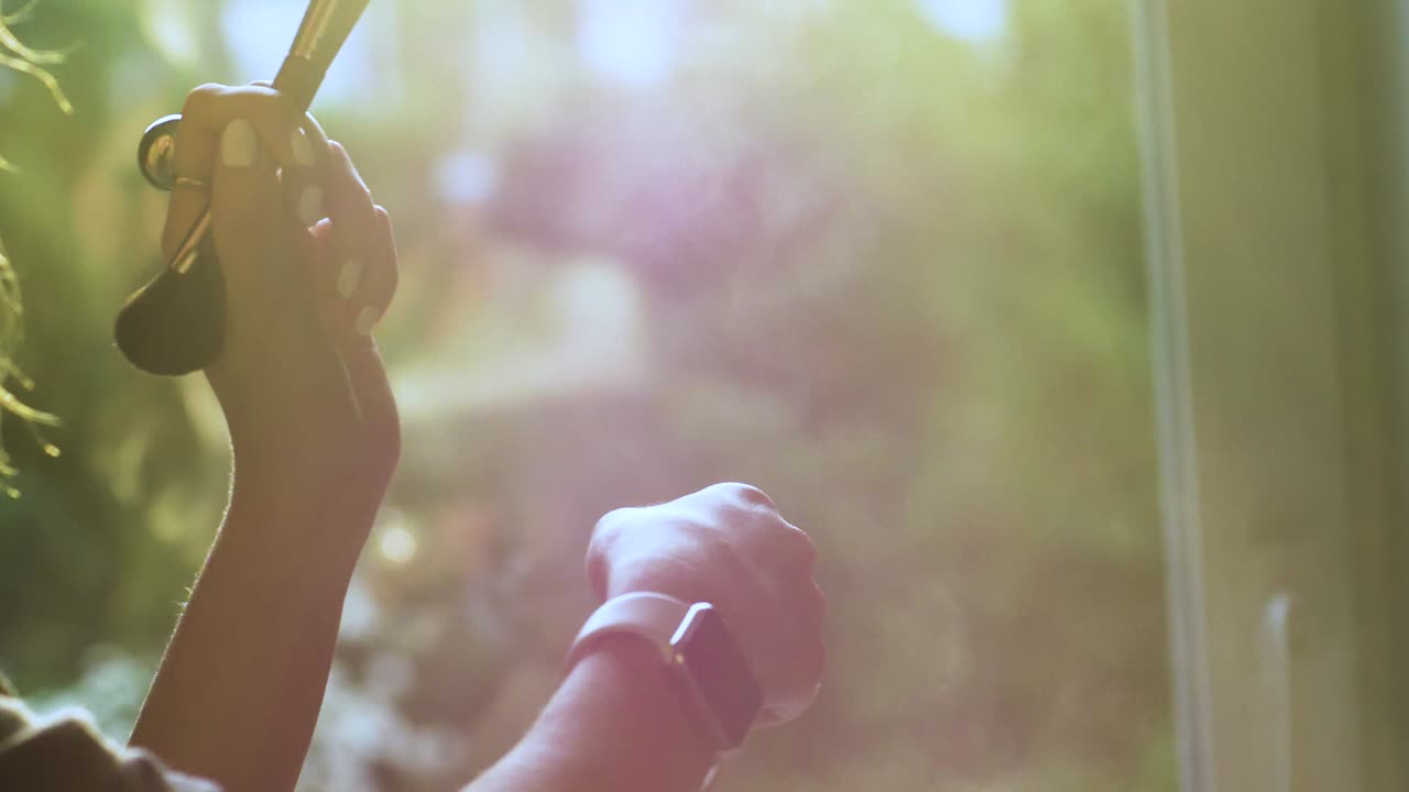 메이크업 아티스트가 메이크업 브러시로 손목을 때리고 햇빛에 파우더 스플래쉬를 만듭니다.