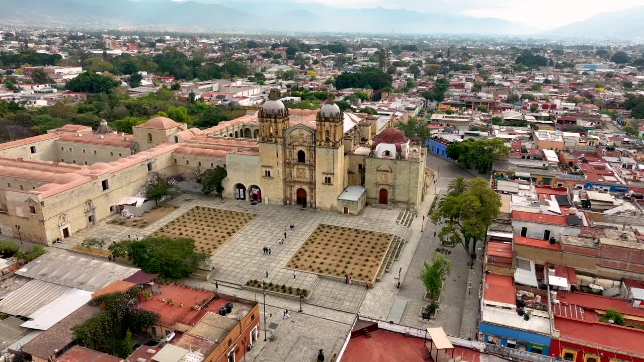 Drone orbit around Santo Domingo Temple in Oaxaca City. Wide daytime view of the historic church, courtyard, and surrounding streets with few people