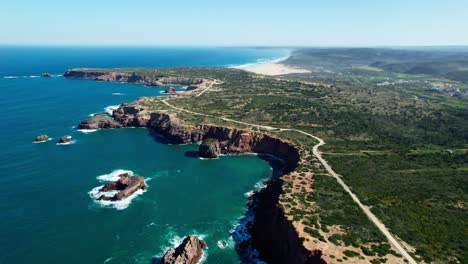 rocky cliffs by the blue sea with winding roads and green hills. - aerial shot