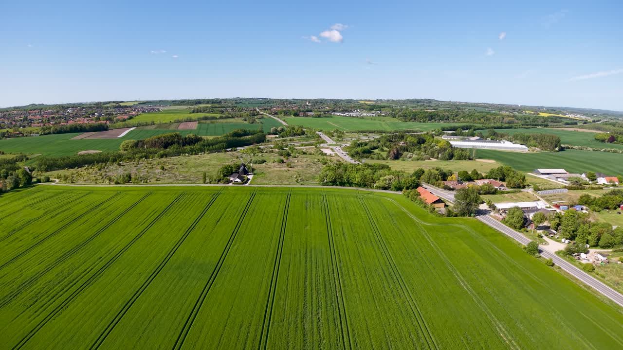 Drone shot of green agricultural fields and scattered farmhouses under a clear sky
