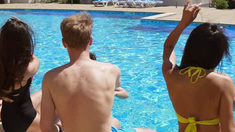 Fröhliche-Gruppe-Junger-Freunde,-Die-Im-Sommer-Am-Pool-Sitzen,-Cocktails-Trinken,-Sich-Unterhalten-Und-Tanzen.-Schwimmbad