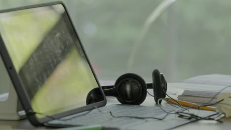 a tablet with headphones and notebooks sit on a table for virtual learning