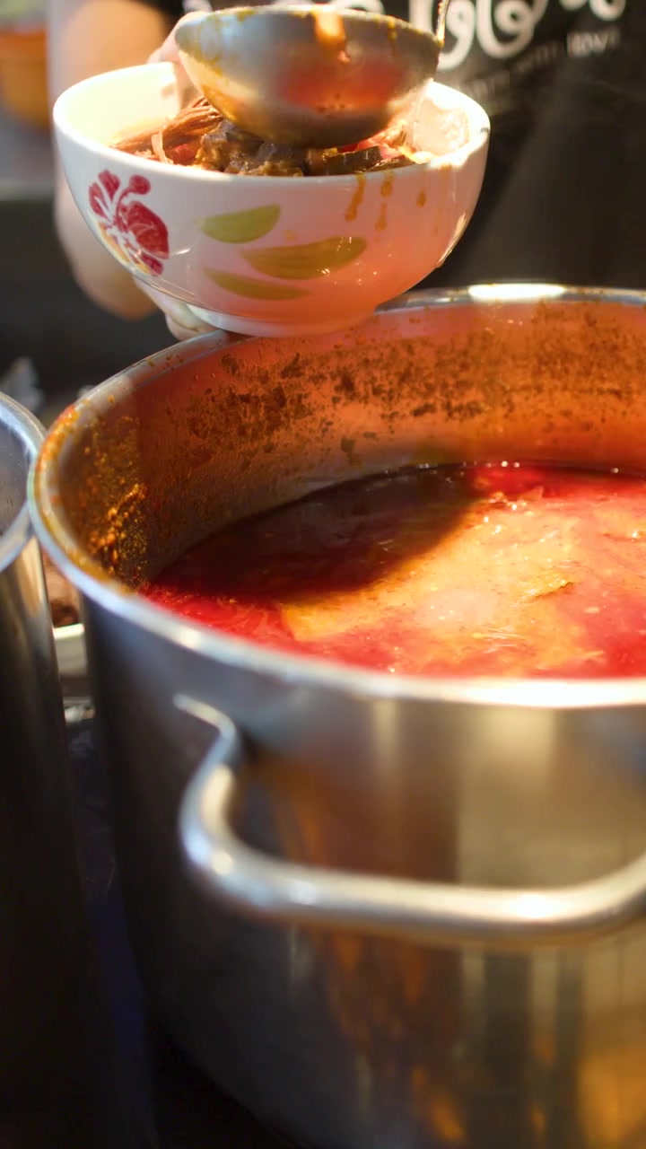 Un primo piano mostra un mestolo che raccoglie curry rosso piccante in una ciotola di ceramica