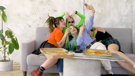 happy women taking selfie while holding beers on a sofa at pizza party