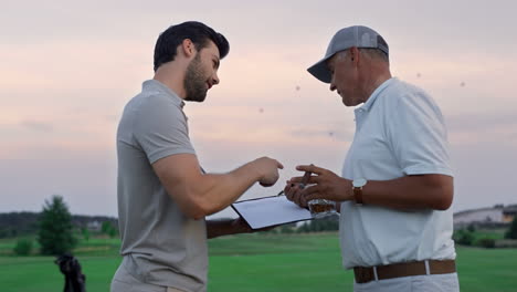 Two-golfers-communicate-outside-on-sunset-fairway.-Golf-group-talk-in-sportswear