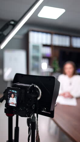 approaching a modern camera on tripod filming a female speaker. day light lamp stands near on the stand. blogging concept. blurred backdrop. vertical video.