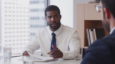 two businessmen sitting around table meeting in modern open plan office