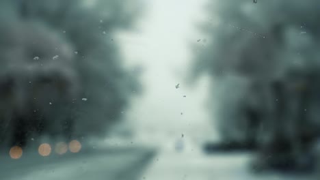 inside view of the front windshield of a car with wet snow falling onto it and windshield wipers cleaning it off