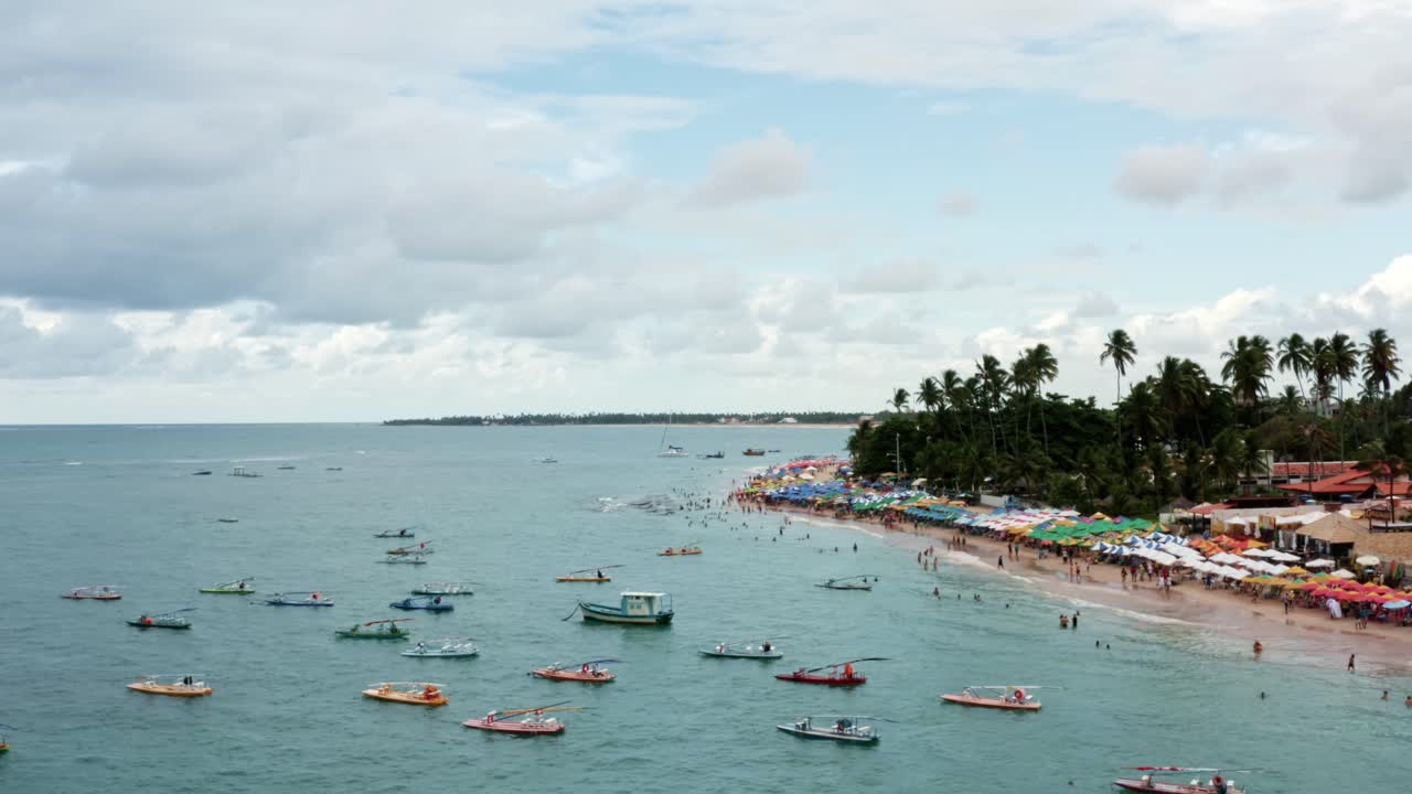 a la izquierda, un camión aéreo con drones tomó la playa de porto de galinhas o chicken port con veleros anclados, sombrillas coloridas y turistas nadando en las aguas cristalinas del océano en pernambuco, brasil.
