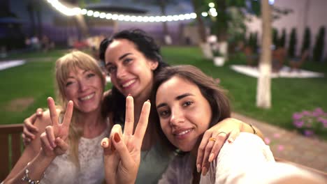 three attractive women met in veranda cafe outdoors taking selfie photo or video on smartphone