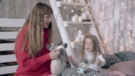 blond mother and daughter play with christmas toys on bed