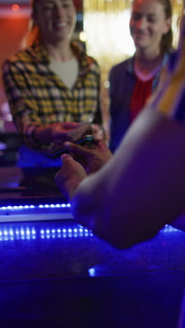 vertical video of two happy caucasian female friends making credit card payment at a bar
