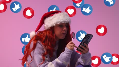 gen z mulher vestindo chapéu de papai noel comendo pirulito de doces olhando para o telefone móvel com emojis de gráficos de movimento mostrando várias notificações de mídia social gostando e reagindo ao conteúdo on-line 2