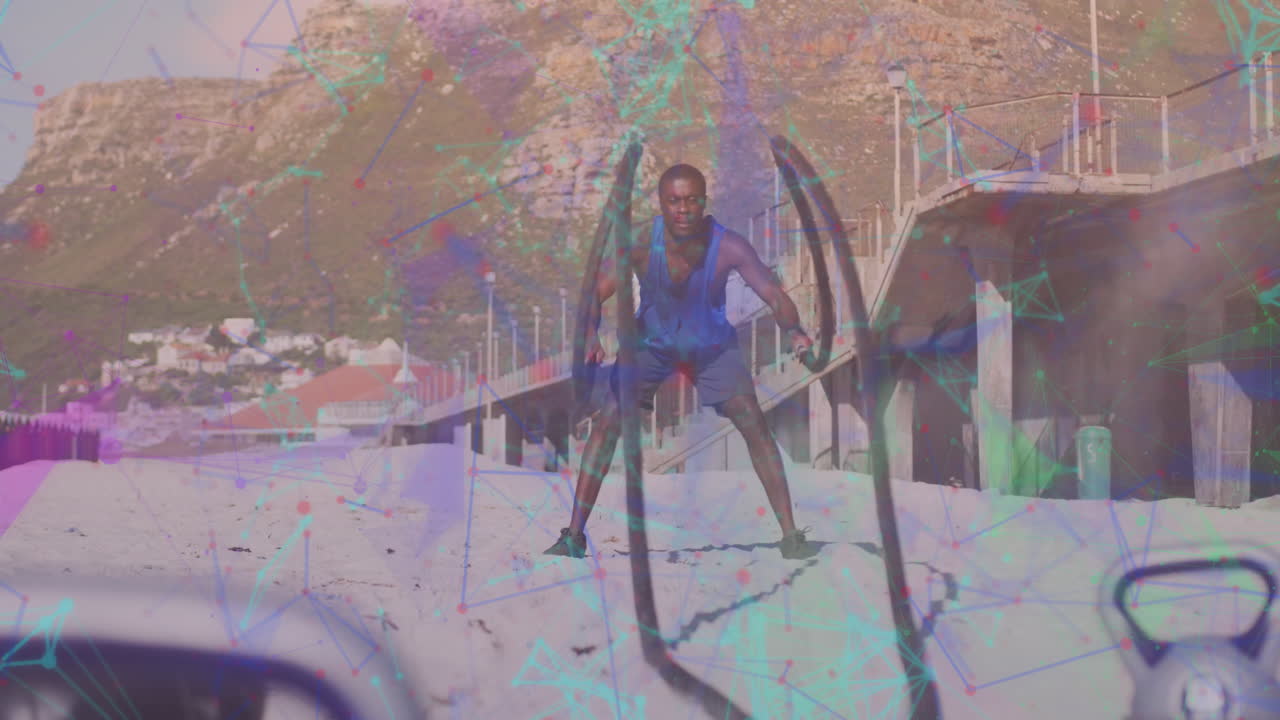 un hombre afroamericano hace ejercicios con una cuerda en la playa, mostrando tecnología deportiva.