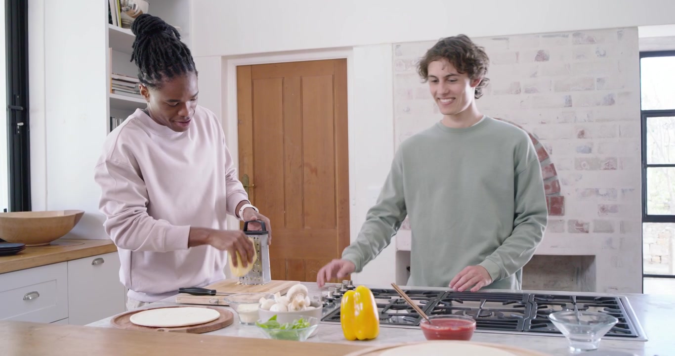 Diverse friends entering from doorway starting pizza prep, African American woman using box grater