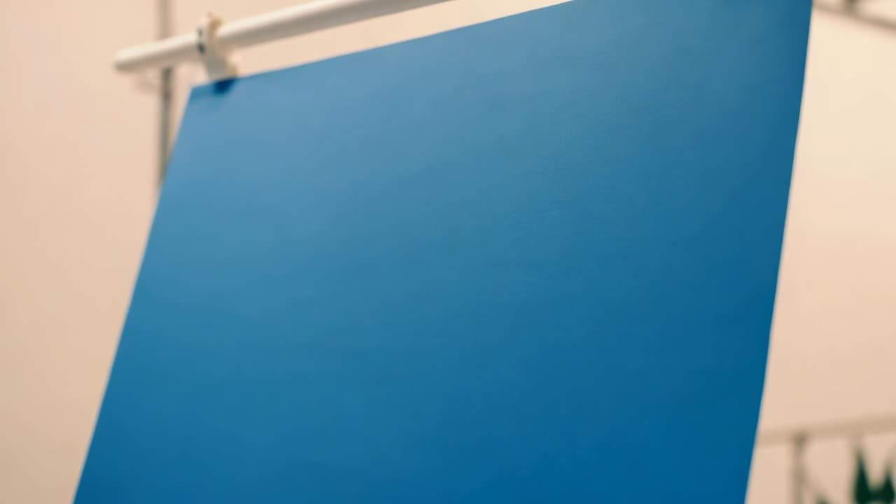 Afastando a câmera, revelando o plano de fundo azul pendurado em uma barra branca em um estúdio pequeno, mostrando os clipe