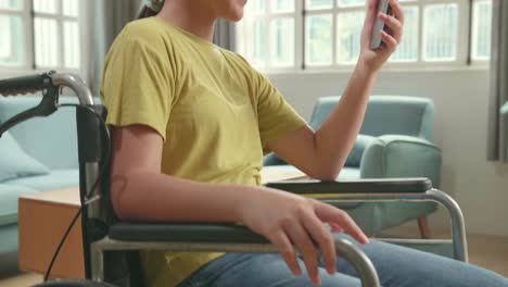close up of asian kid girl sitting in a wheelchair while waving hand video calling distance friend online in mobile chat app at home